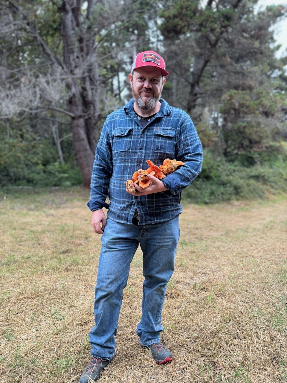 Richard Gregory standing in a mown meadow holding an armful of bright orange lobster mushrooms