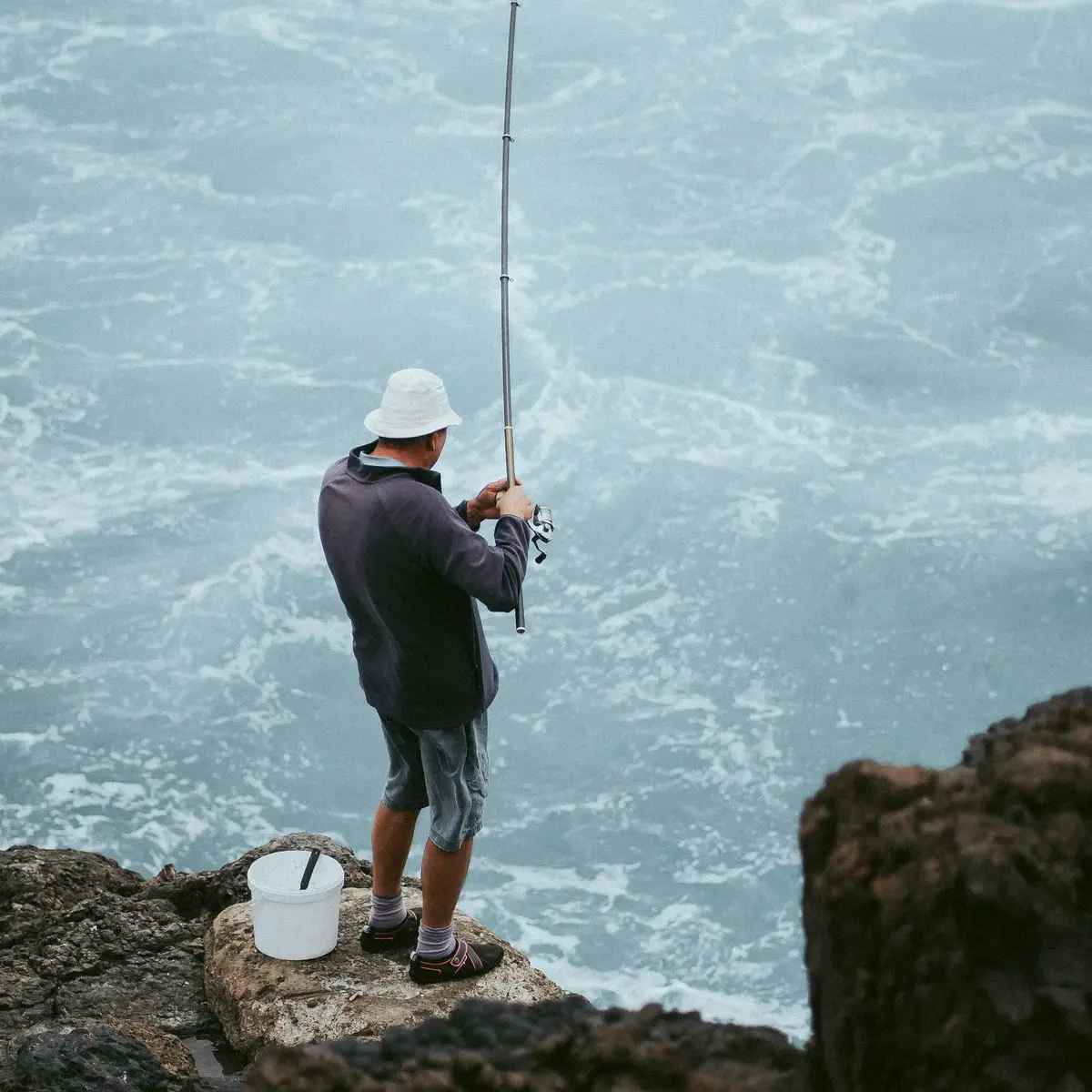 An angler casting from the rocks into heavy surf
