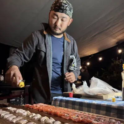 Taku Kondo of Outdoor Chef Life laying out sashimi on a board under the tarp at camp
